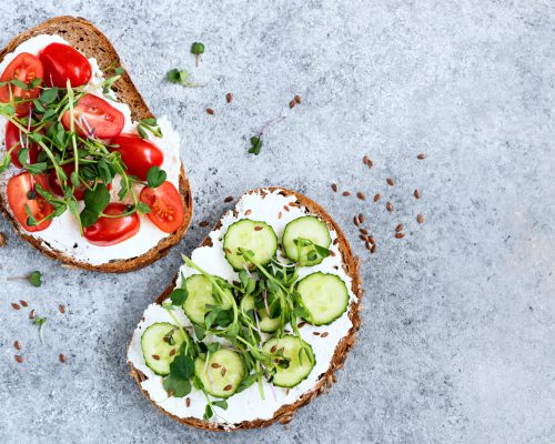 Healthy vegetarian toasts with cream cheese, cucumber, cherry tomato and micro greens on top. Table top view on concrete backdrop. Copy space