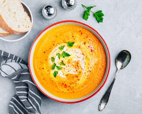 Carrot and pumpkin cream soup with parsley on gray stone background. Top view, copy space