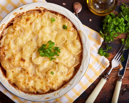 Potato gratin. Slices of potato backed with cream sauce, garlic and cheese, decorated with parsley leafs. Top view. Rustic style. Vegetarian dish.