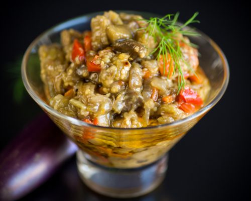 cooked summer eggplant caviar with vegetables in a bowl isolated on black background