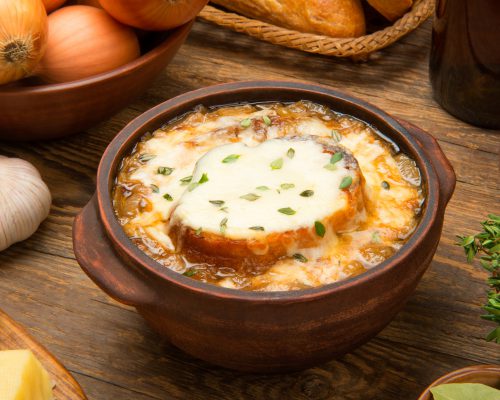 French onion soup in a bowl on a wooden table.