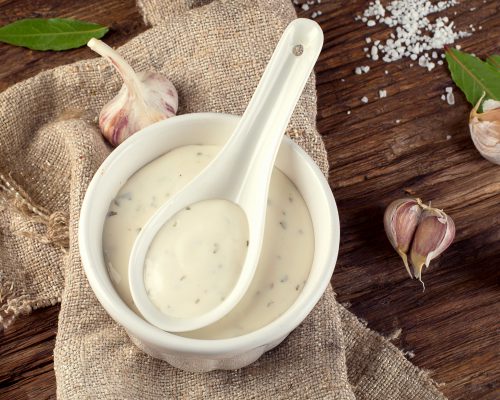 Bowl of Garlic sauce or mayonnaise on a wooden board.